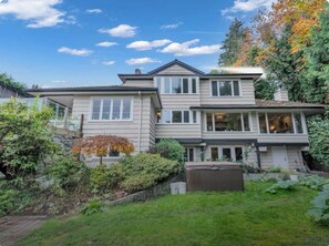 A two-story house with a front yard, a stone wall, and a large window on the upper floor. - Luxury Accommodation in West Van (West Vancouver)