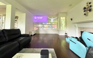 A living room with a large screen displaying a sports channel, a fireplace, and a seating area with sofas. - Luxury Accommodation in West Van (West Vancouver)