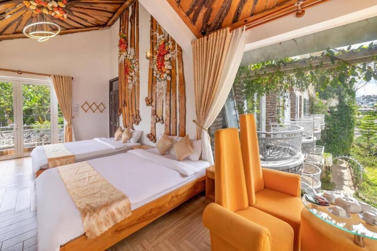 A bedroom with a bed, two chairs, a glass table, and a view of greenery.