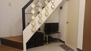 Een trap met een uniek golvend hekwerk, een flatscreen-tv en een speakersysteem in een kamer met een betegelde vloer.