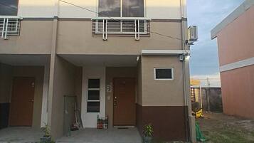 Un edificio de dos pisos con techo plano, un balcón en el segundo nivel y una ventana pequeña en la planta baja.
