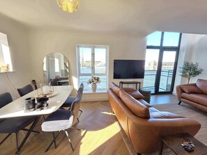 Ein modernes Wohnzimmer mit Essbereich, einer Couch, einem Fernseher und Blick auf das Wasser.