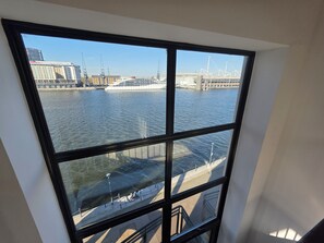 A view through a window of a river with buildings and a bridge in the background. - Bright Modern 2BR Flat Sleeps 5 Royal Docks (Greater London)