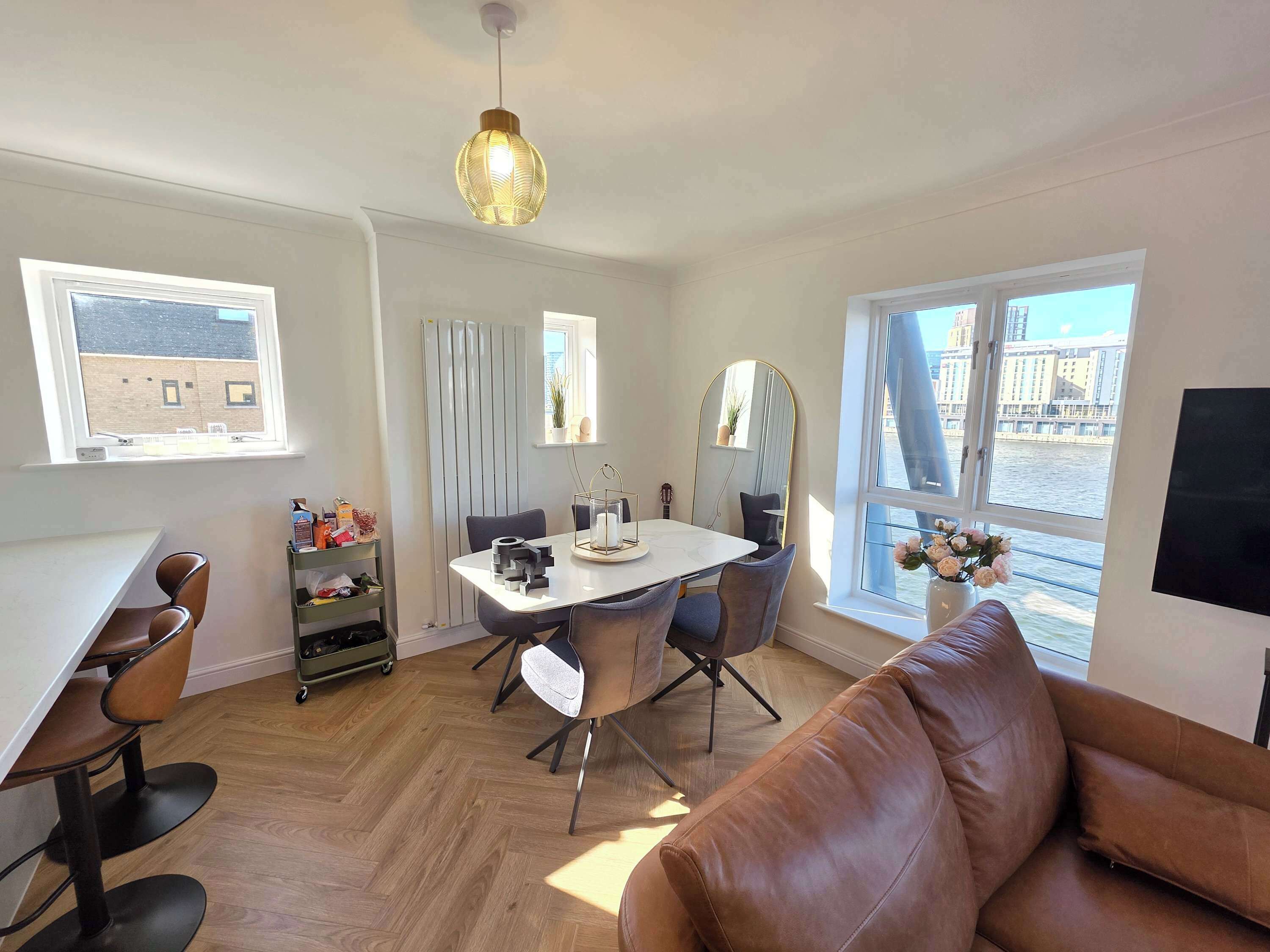 A modern living room with a dining table, leather sofa, and large windows with a view of buildings.