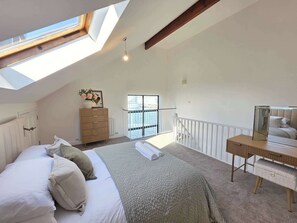 Ein Schlafzimmer mit Oberlicht, Bett, Kommode, Schreibtisch und einem Balkon mit Blick auf das Wasser.