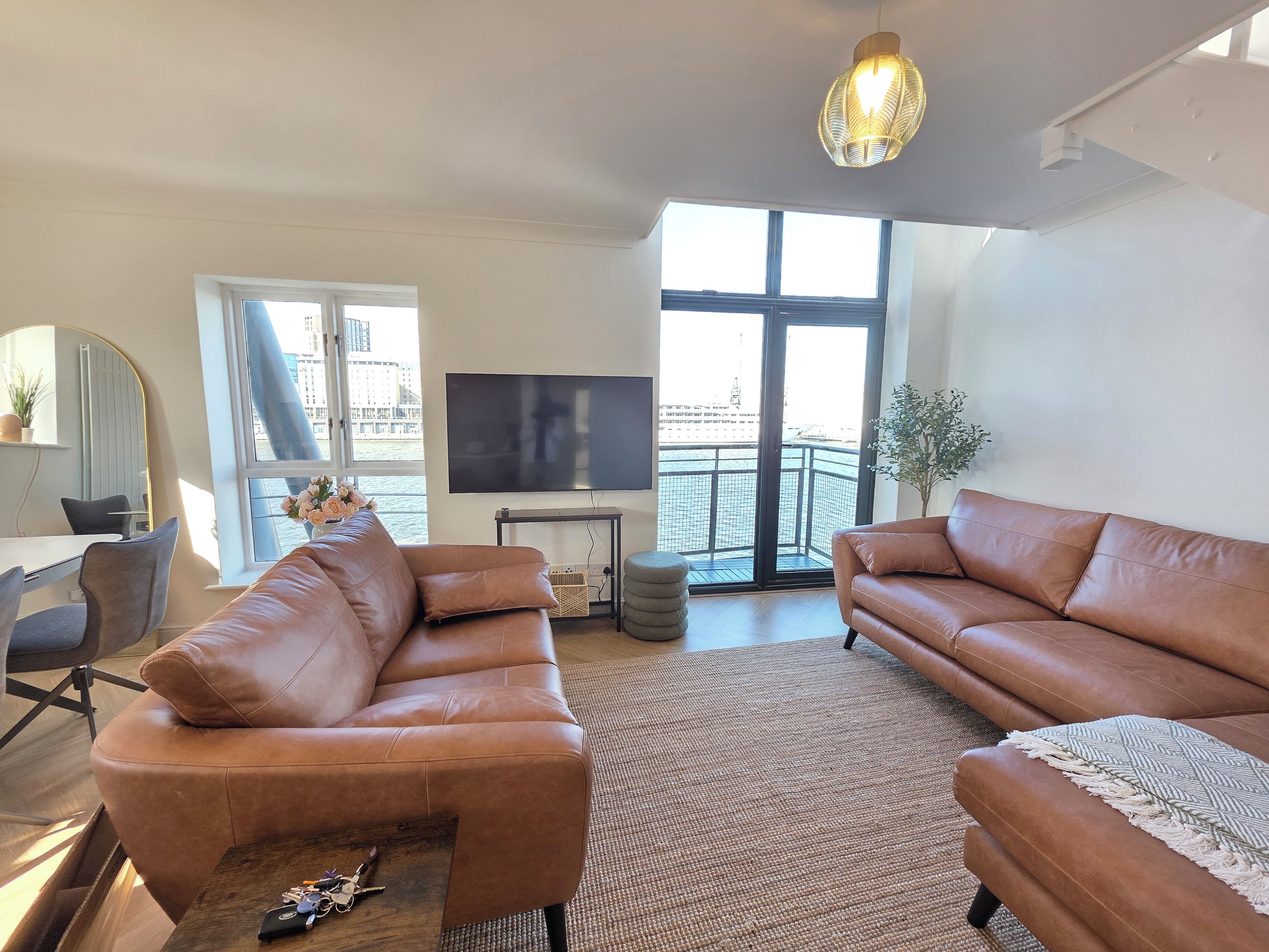 A modern living room with leather sofas, a flat-screen TV, and a large window overlooking a balcony.