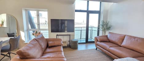 A modern living room with leather sofas, a flat-screen TV, and a large window overlooking a balcony.