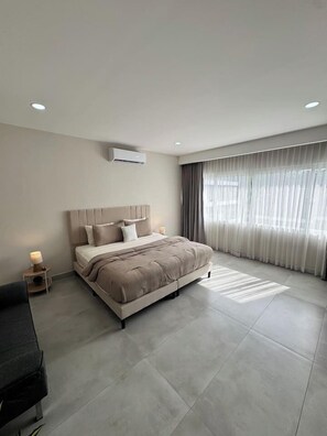 A modern bedroom with a large bed, a bedside table, an air conditioning unit, and a window with curtains. - Private Pool Home for 8 | 5 Min to Jacó | 87 (Jaco)