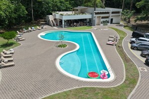 A swimming pool with a unique curved design, surrounded by lounge chairs and a covered seating area. - Private Pool Home for 8 | 5 Min to Jacó | 87 (Jaco)