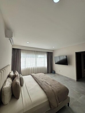 Een moderne slaapkamer met een groot bed, een flatscreen televisie aan de muur en een groot raam met gordijnen.