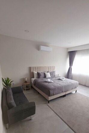Ein modernes Schlafzimmer mit Bett, Sofa, Nachttisch und Topfpflanze.