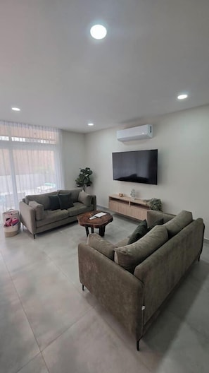 A modern living room with a flat-screen TV, two sofas, a coffee table, and a large window with sheer curtains. - Private Pool Home for 8 | 5 Min to Jacó | 87 (Jaco)