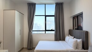 Una habitación de hotel con cama, armario, ventana con cortinas y vista a la ciudad.