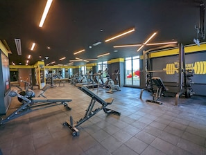 Uma academia com equipamentos de exercícios, janelas amplas e uma área de musculação.