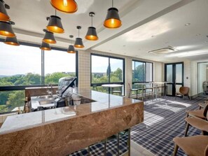 A modern kitchen with a large island, a dining area with chairs, and large windows offering a view of the outdoors. - Luxury 2 BR Loft w Pool, Patio & Menlyn Maine (Pretoria)