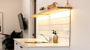 Une cuisine compacte dotée d’un évier encastré, d’une étagère ornée d’objets décoratifs et d’une plante en pot.