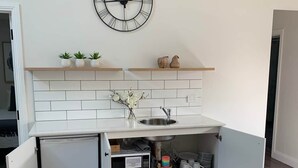 Une cuisine compacte équipée d’un four à micro-ondes encastré, d’un évier et d’une horloge murale.