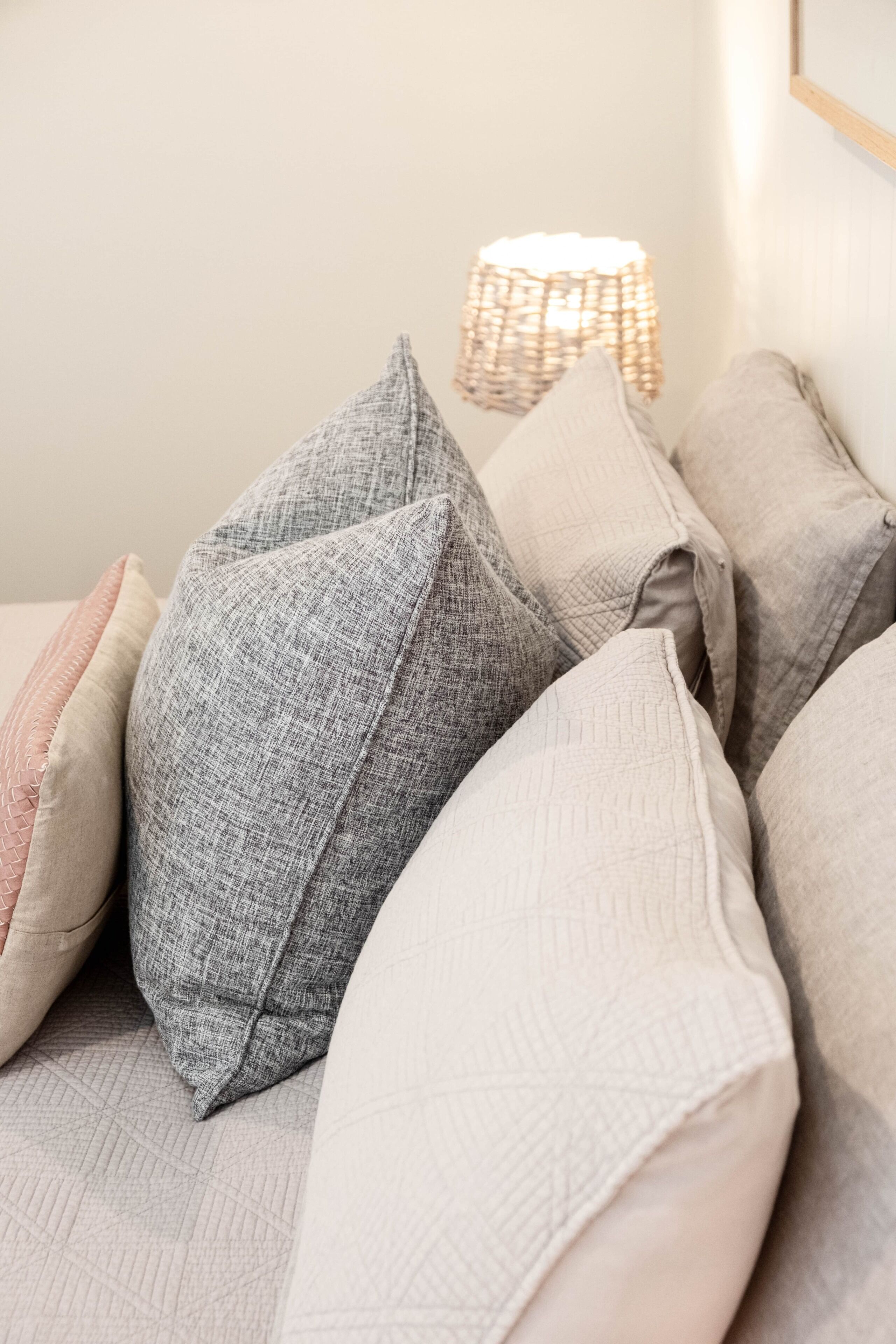 A close-up of a bed with multiple pillows and a woven lamp.