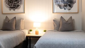 Une chambre avec deux lits, une table de chevet avec une lampe, deux petites plantes en pot et deux œuvres d’art florales encadrées accrochées au mur.