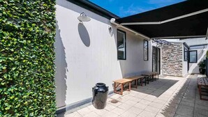 Une terrasse avec un mur en pierre, un banc en bois et un grand bac noir.