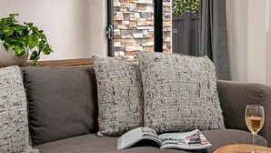 Un canapé gris agrémenté de coussins à motifs, un magazine et un verre de vin posés sur une petite table en bois.