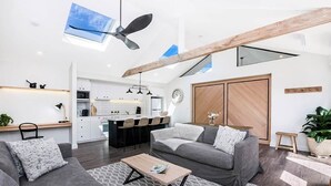 Un espace de vie moderne comprenant une cuisine, des canapés gris, une table basse et une poutre en bois au plafond.