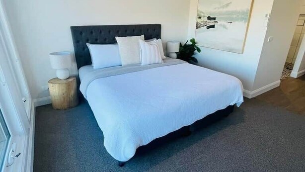 Ein Schlafzimmer mit einem großen Bett, einem Nachttisch mit Lampe, einer Wand-Klimaanlage und einem gerahmten Bild an der Wand.