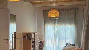 A bedroom with a bed, a wardrobe, a desk, a chair, a hanging light fixture, and a window with curtains. - Large Guesthouse 80m in lovely Ramot (Ramot)