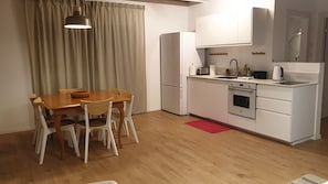 A compact kitchen with a dining table, chairs, a refrigerator, an oven, and a sink.