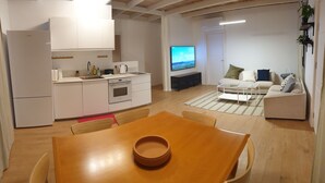 A modern kitchen with white cabinets, a dining table with chairs, a sofa, and a TV in the living area. - Large Guesthouse 80m in lovely Ramot (Ramot)