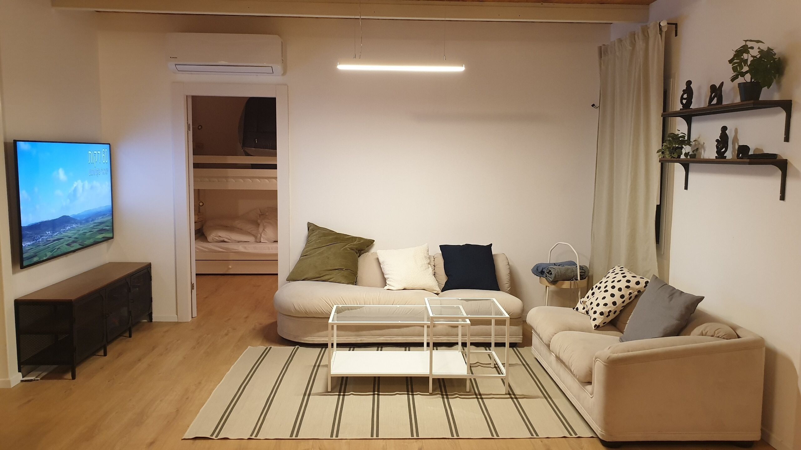 Een woonkamer met een bank, een salontafel, een televisie, een kledingkast en een plank met decoratieve objecten.
