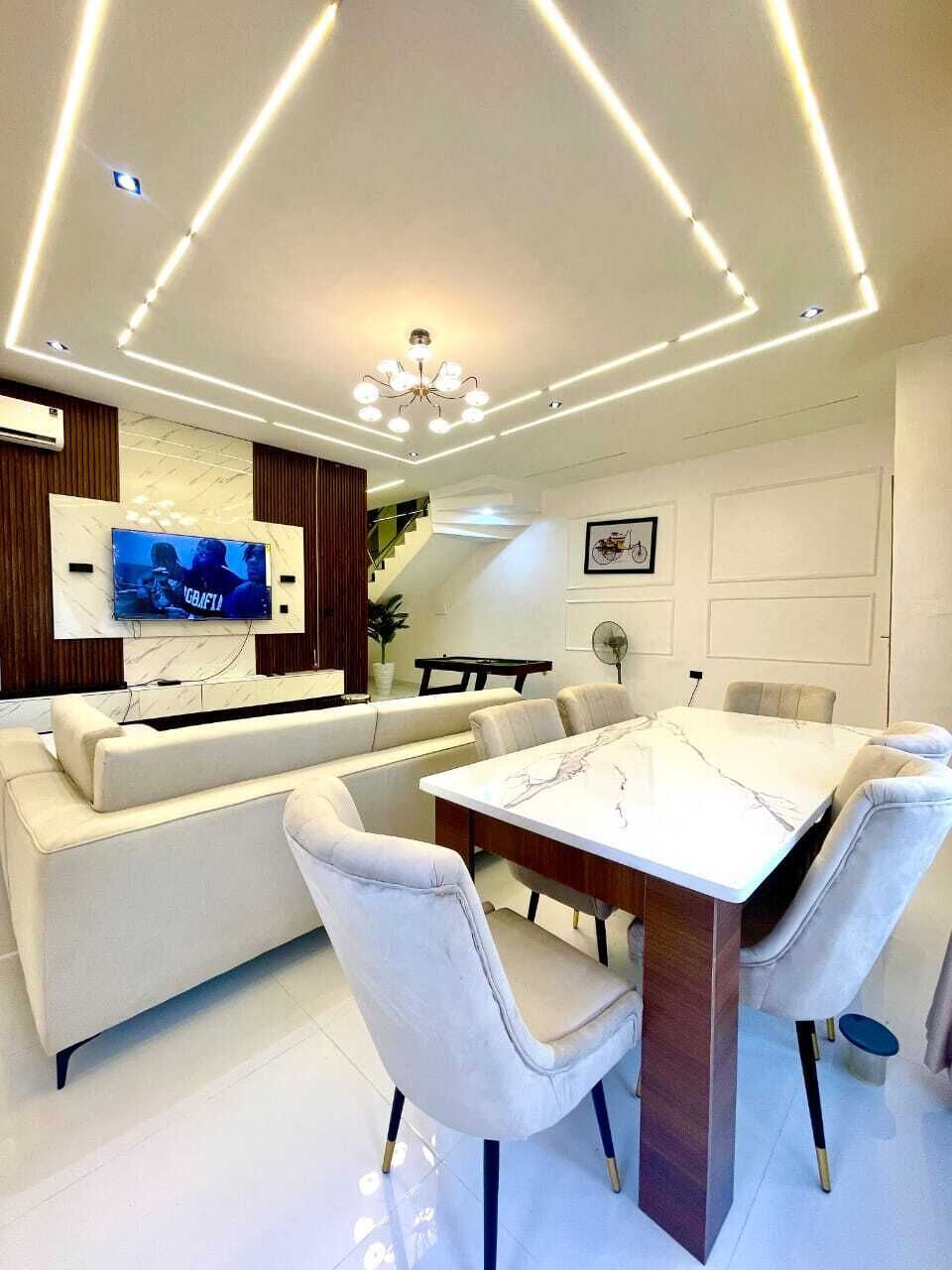 Un espace repas moderne avec une table en marbre, des chaises à revêtement blanc, un canapé et un téléviseur fixé au mur.