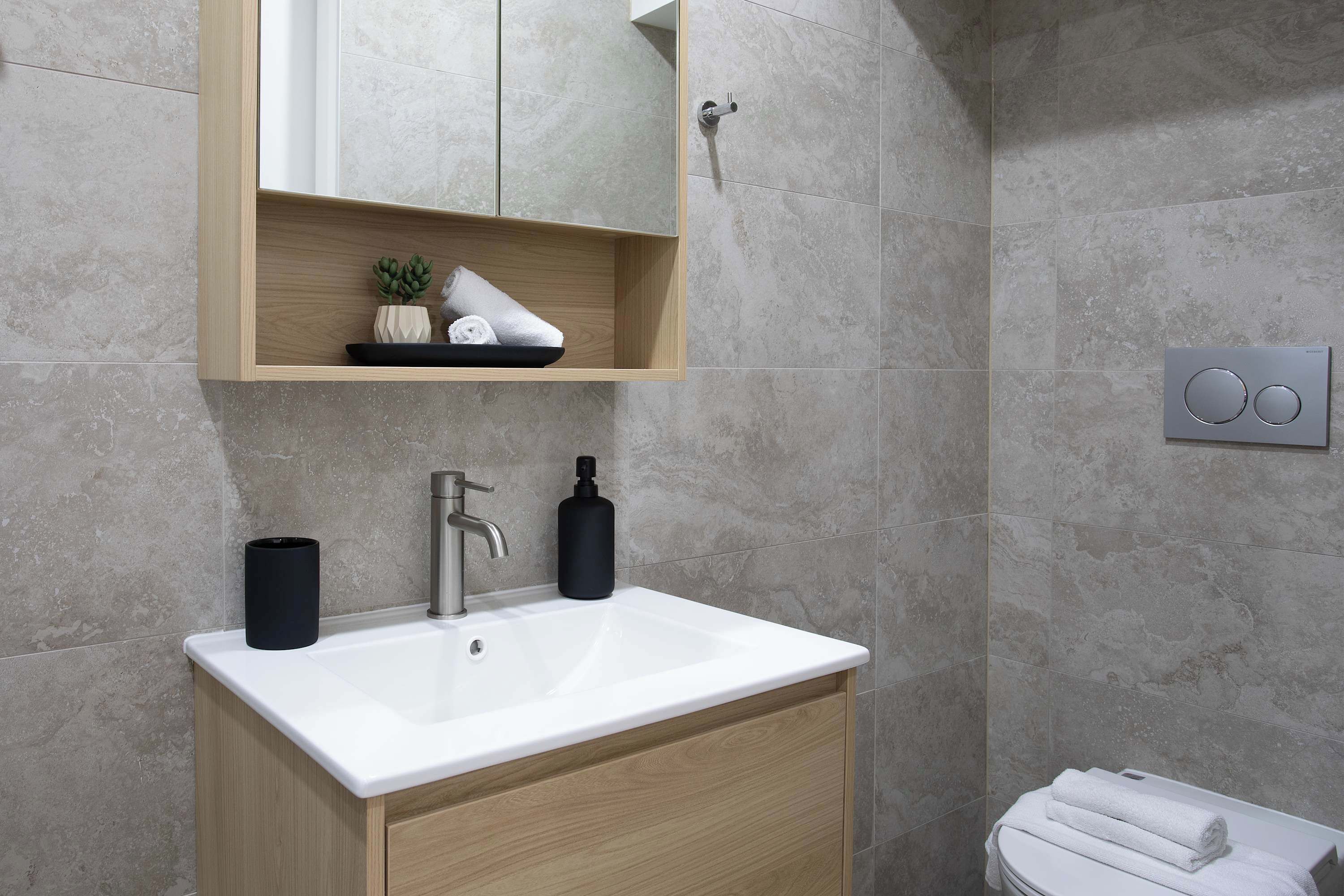 A modern bathroom with a white sink, wooden cabinet, and a mirror above.