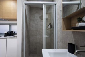 Ein modernes Badezimmer mit Duschkabine aus Glas, einem weißen Waschbecken und einem Holzboden mit Handtuch.