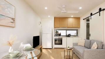 A compact living space with a dining area, a sofa, a kitchen with a microwave and oven, and a ceiling fan.