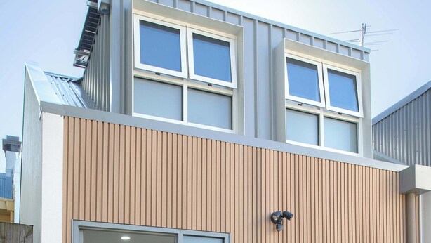 Un bâtiment moderne à deux étages, avec une cuisine visible à travers une porte vitrée.