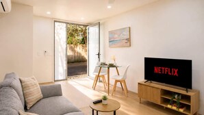 Un salon moderne comprenant un canapé, une table basse, un téléviseur et un coin repas avec des chaises et une table en verre.