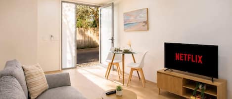 Una sala de estar moderna con un sofá, una mesa de centro, un televisor y un comedor con sillas y una mesa de vidrio.