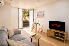 A modern living room with a sofa, a coffee table, a TV, and a dining area with chairs and a glass table. - The Loft | Charming 1BR Glebe, Near Sydney Uni (Glebe)