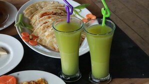 Una mesa con una fuente de panes planos y dos vasos de jugo verde.