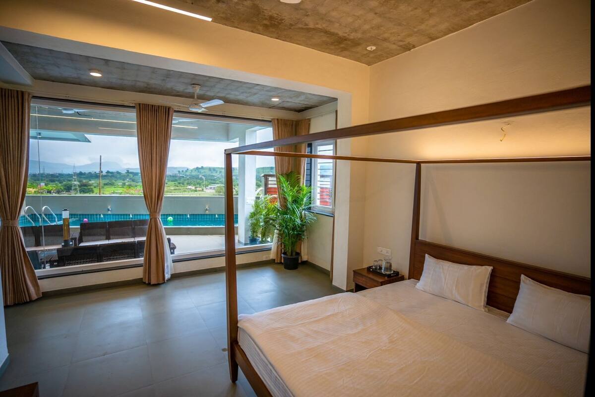 Ein Schlafzimmer mit Himmelbett, Blick auf einen Pool und einem Balkon mit Vorhängen.