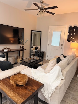Ein Wohnzimmer mit Sofa, Couchtisch, Fernseher, Deckenventilator und einer Tür mit Fenster.