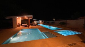 Ein Schwimmbadbereich bei Nacht mit mehreren Pools, einer überdachten Sitzgelegenheit und einem kleinen Gebäude mit Beleuchtung.