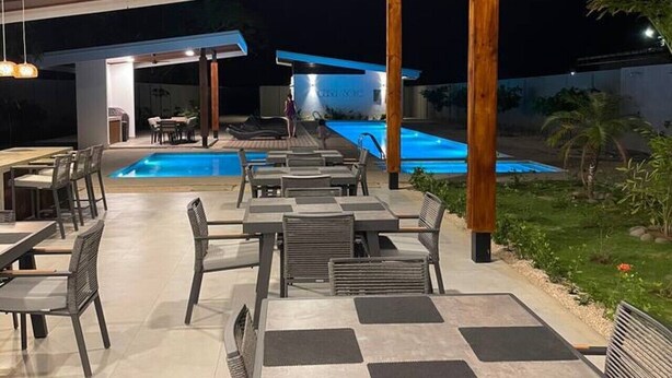 Ein Außenpoolbereich mit Liegestühlen und Tischen, ein überdachter Sitzbereich und ein Pool im Hintergrund.