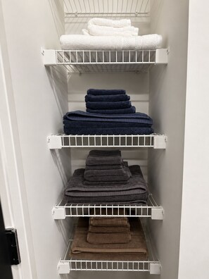Un étagère de rangement où sont pliées avec soin des serviettes blanches, bleu foncé et brunes.
