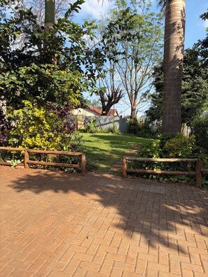 A paved pathway with a wooden fence, surrounded by lush greenery and trees.