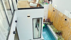 A modern pool area with a glass-enclosed structure, lounge chairs, and a bamboo fence.