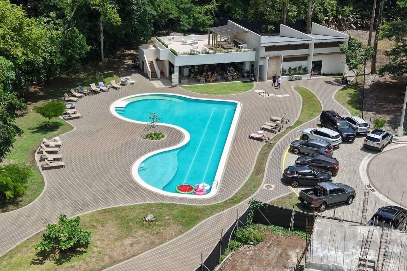 Une piscine avec des chaises longues, un espace de stationnement et un bâtiment doté d’un toit plat.