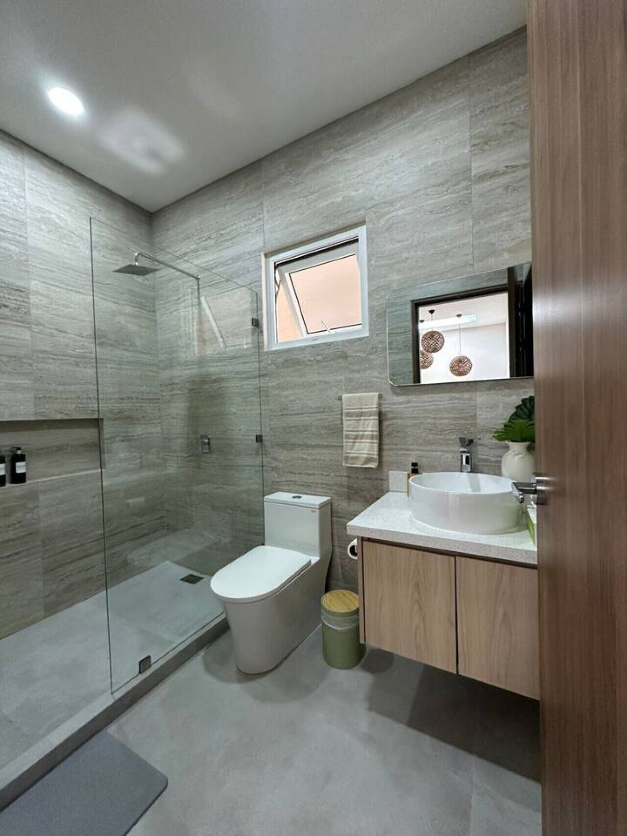 Un baño moderno con cabina de ducha de vidrio, inodoro, lavabo y espejo sobre él.