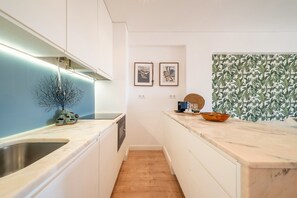 Una cocina moderna con armarios blancos, un lavamanos de acero inoxidable, una encimera de madera y un salpicadero con diseño de hojas. Hay dos cuadros en la pared y una escultura decorativa de árbol sobre la encimera.